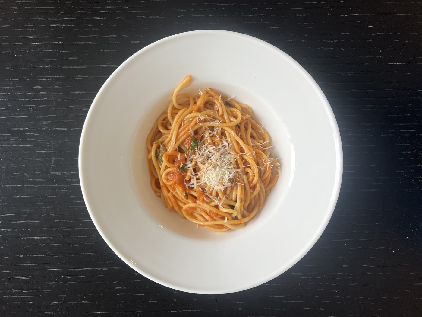 Spaghetti in red tomato sauce with grated cheese in a white bowl