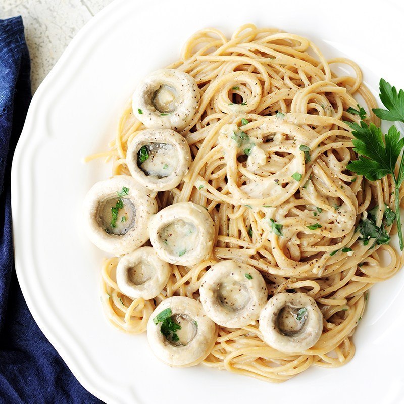 Spaghetti mit heller Sahnesauce und Champignonscheiben auf einem weißen Teller