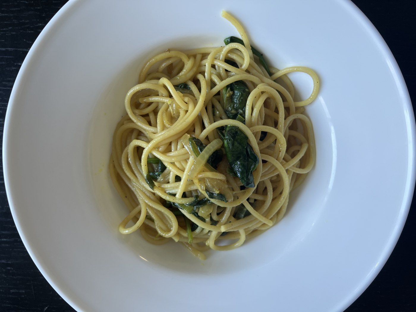 Spaghetti mit grünen Spinatblättern und heller Sahnesauce in einer weißen Schale