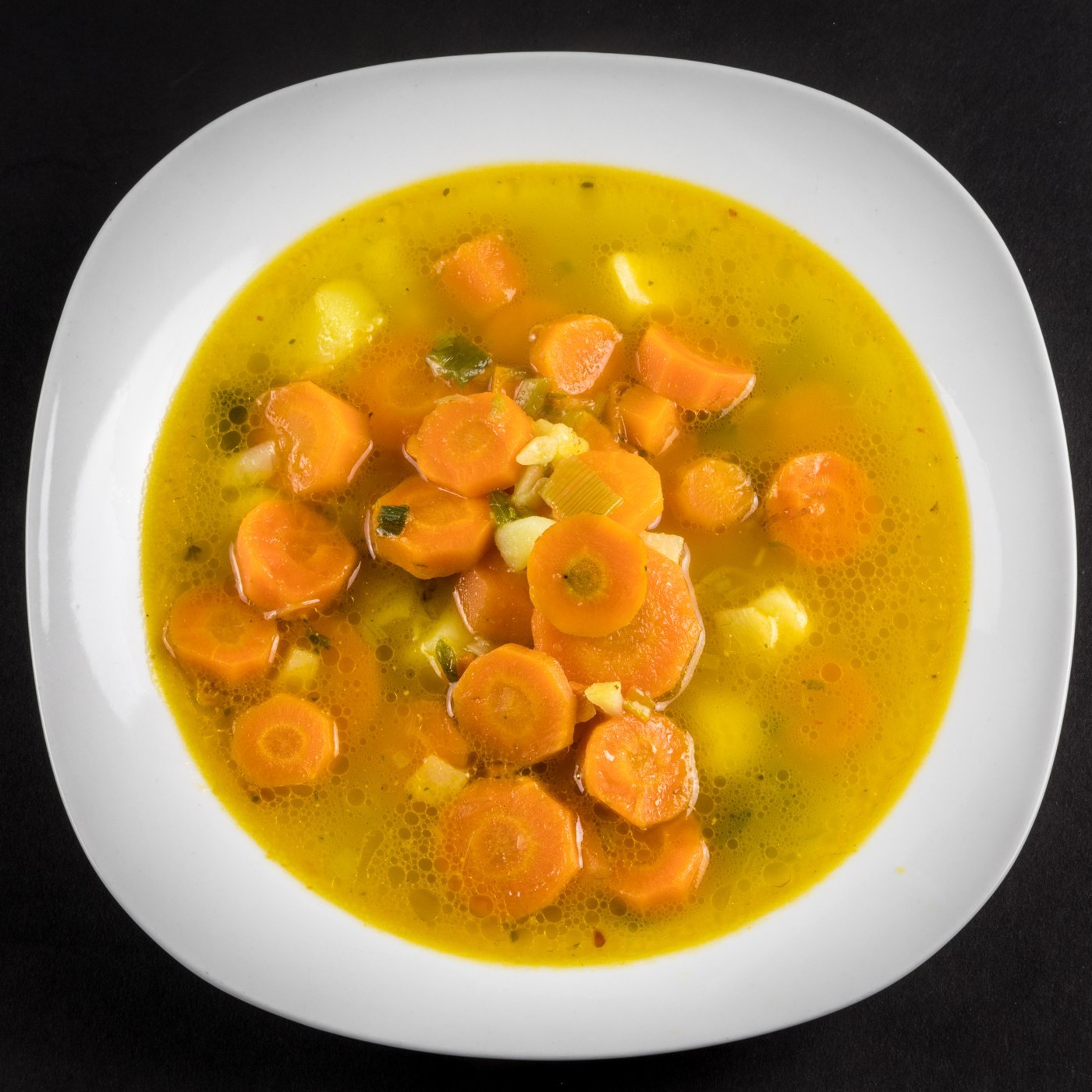 Gelbe Gemüsebrühe mit orangefarbenen Möhrenscheiben und Kartoffelstücken