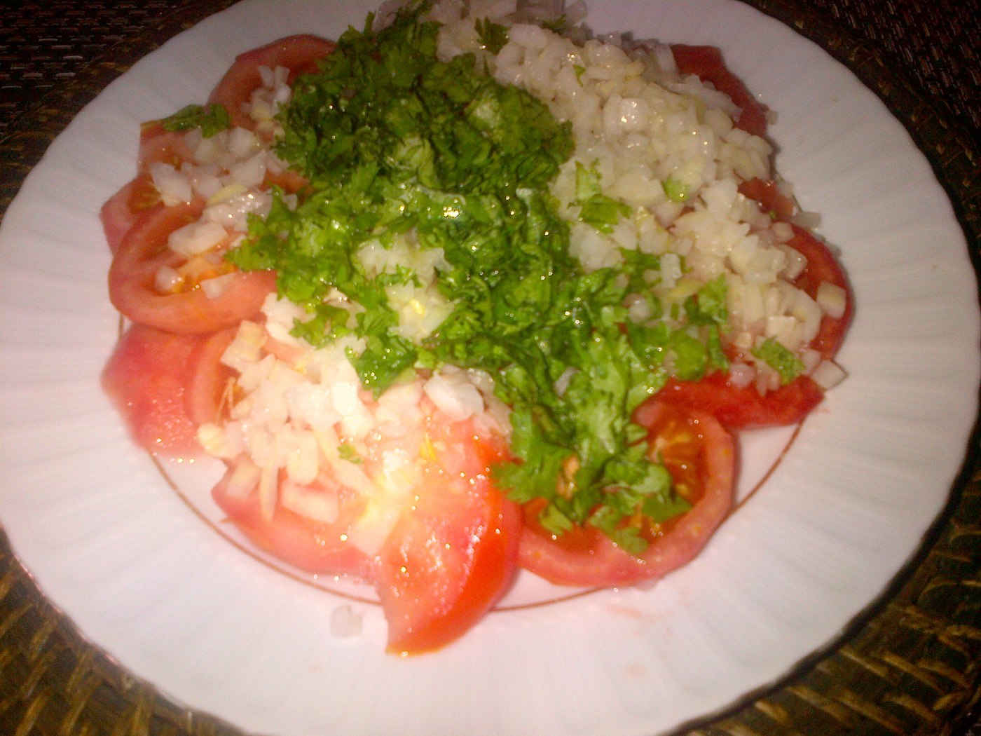 Tomatenscheiben mit fein gehackter Zwiebel und grünen Kräutern auf einer Platte