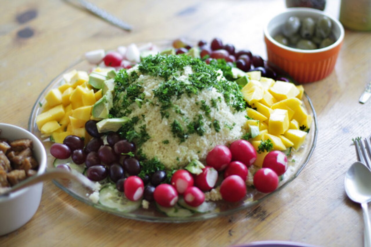 Couscous mit Petersilie, gelber Paprika, Erbsen, roten Bohnen und Radieschen auf einer Platte