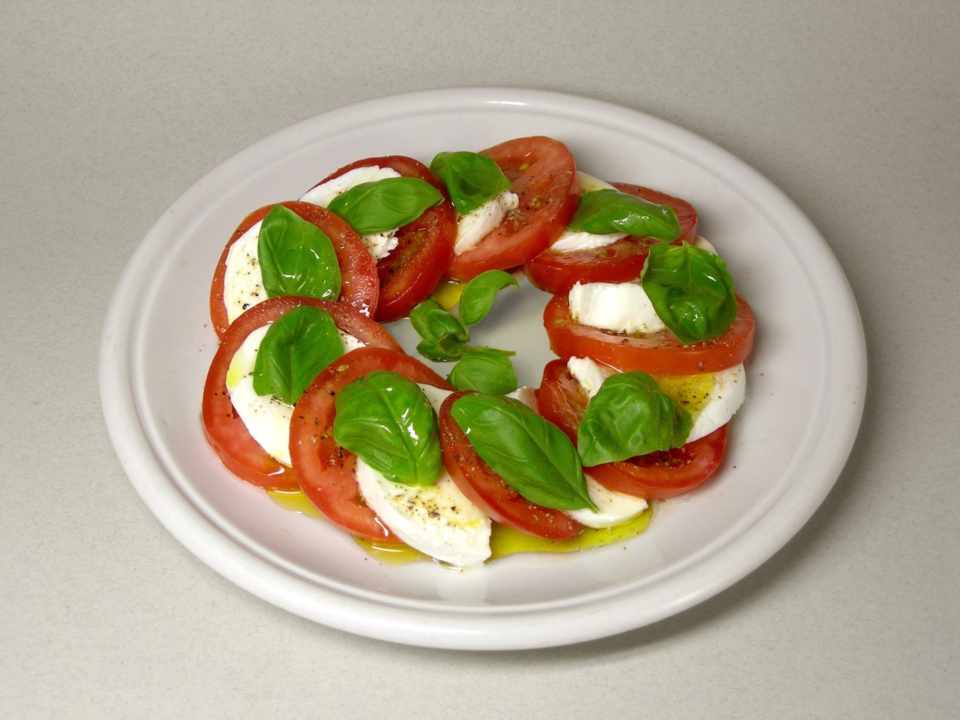 Abwechselnde Tomaten- und Mozzarellascheiben mit ganzen Basilikumblättern