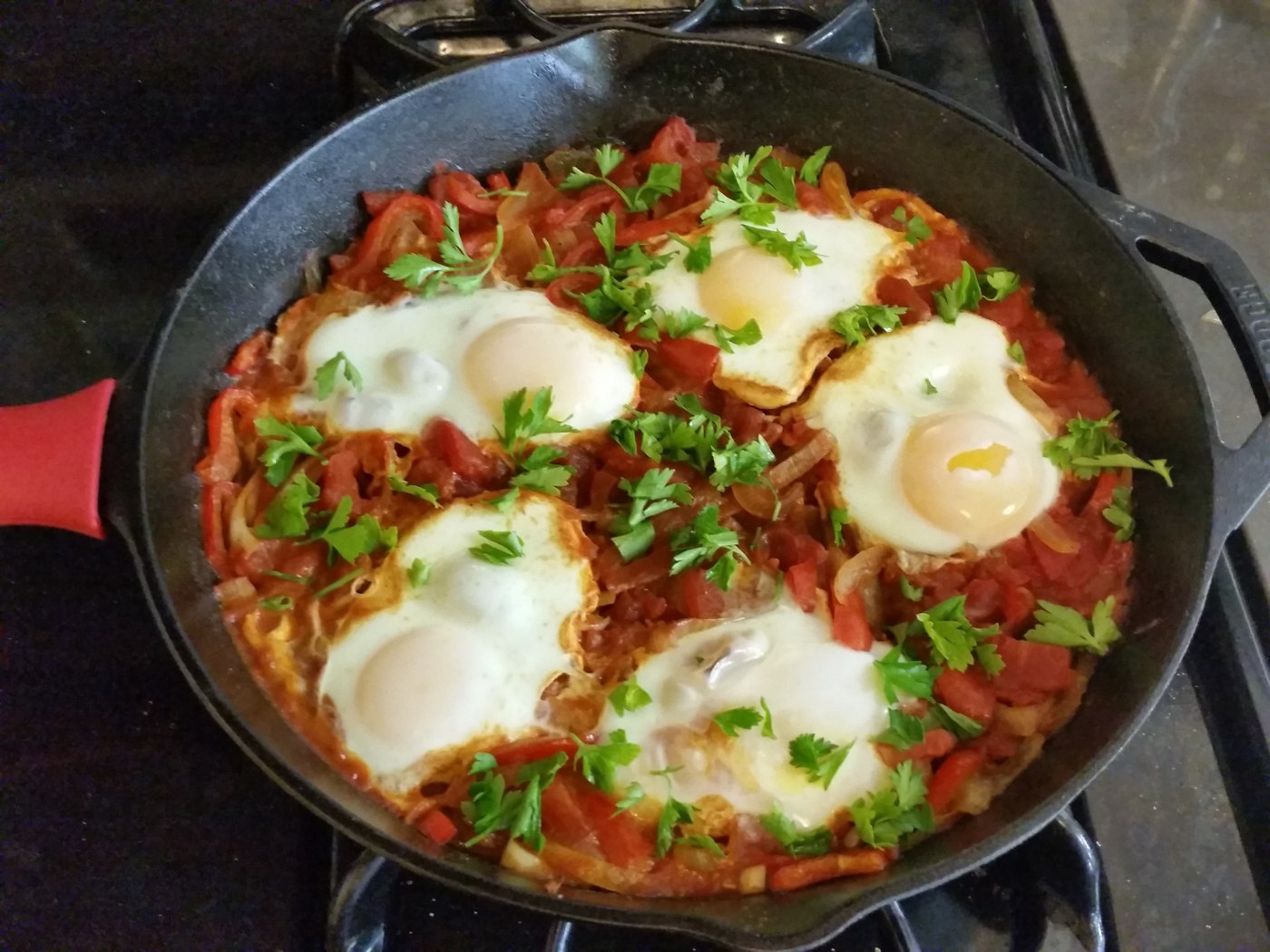 Vier Eier in einer roten Tomaten-Paprika-Sauce mit grünen Kräutern in einer Pfanne