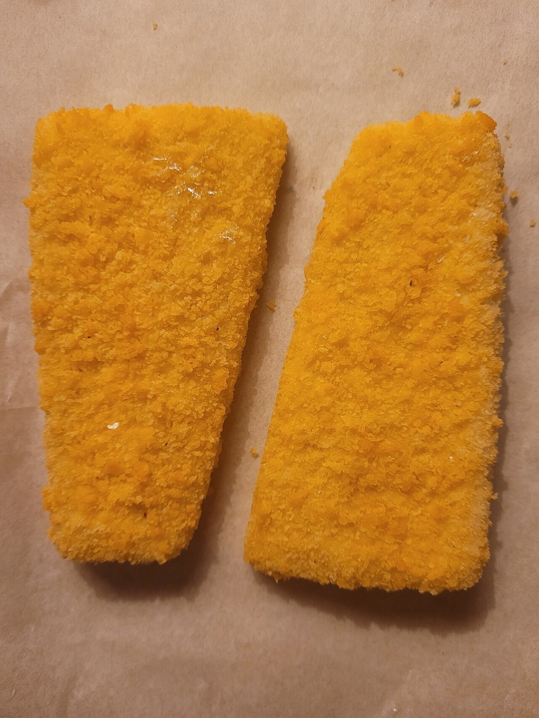 Zwei rechteckige mit goldfarbenen Bröseln panierte Fischstücke vor dem Garen