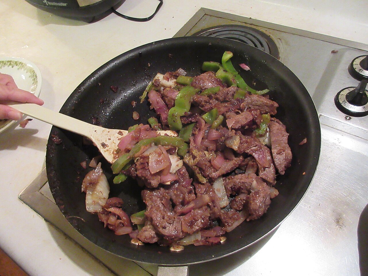 Gebratene Rindfleischstreifen mit grüner Paprika und roten Zwiebeln in einer Pfanne