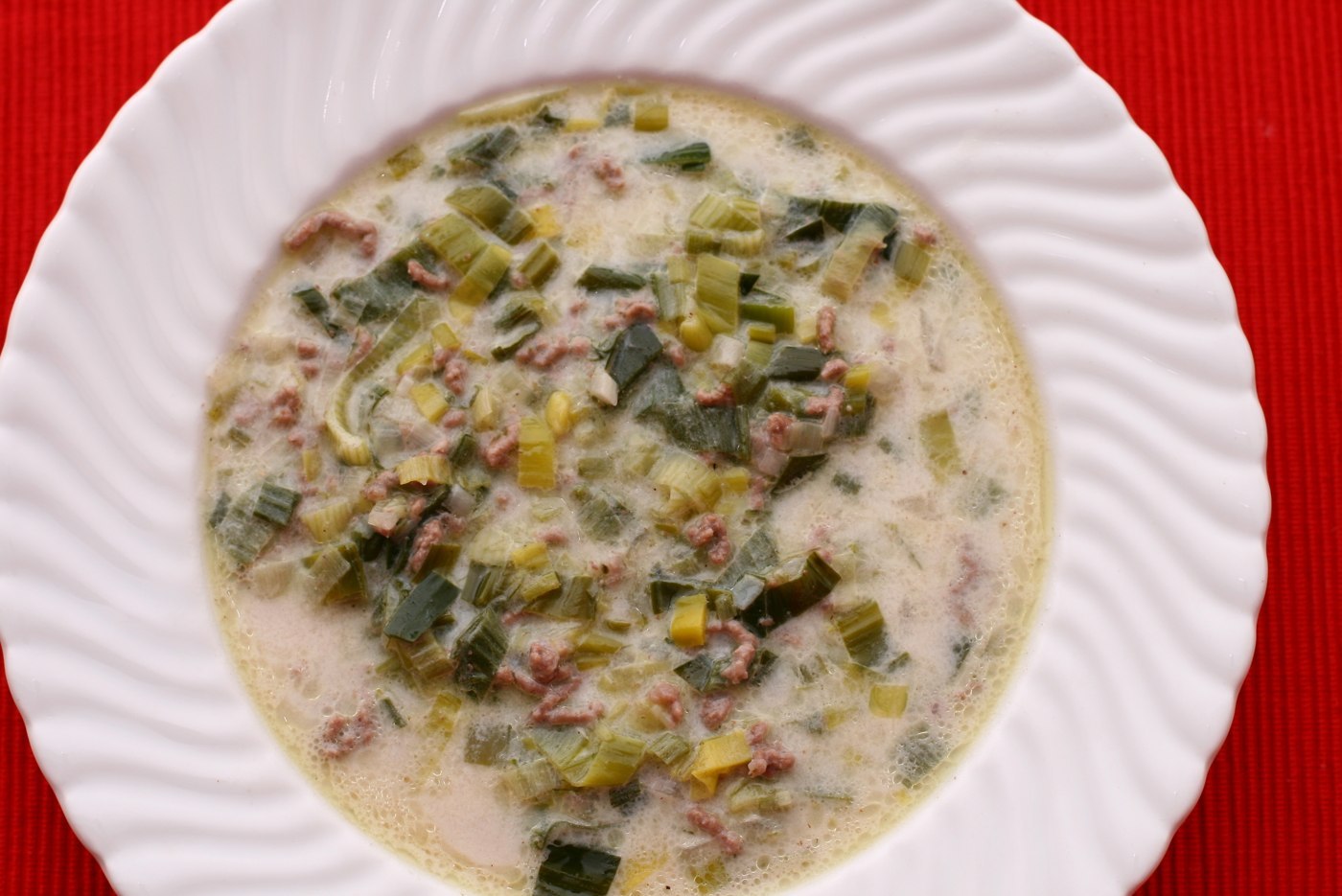 Creamy cheese and leek soup with browned minced meat in a white soup plate