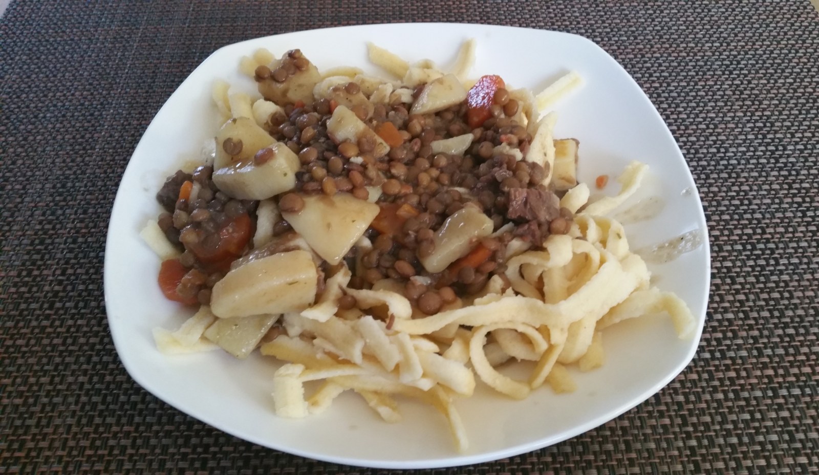 Linsen und Spätzle mit Wurststücken auf einem Teller