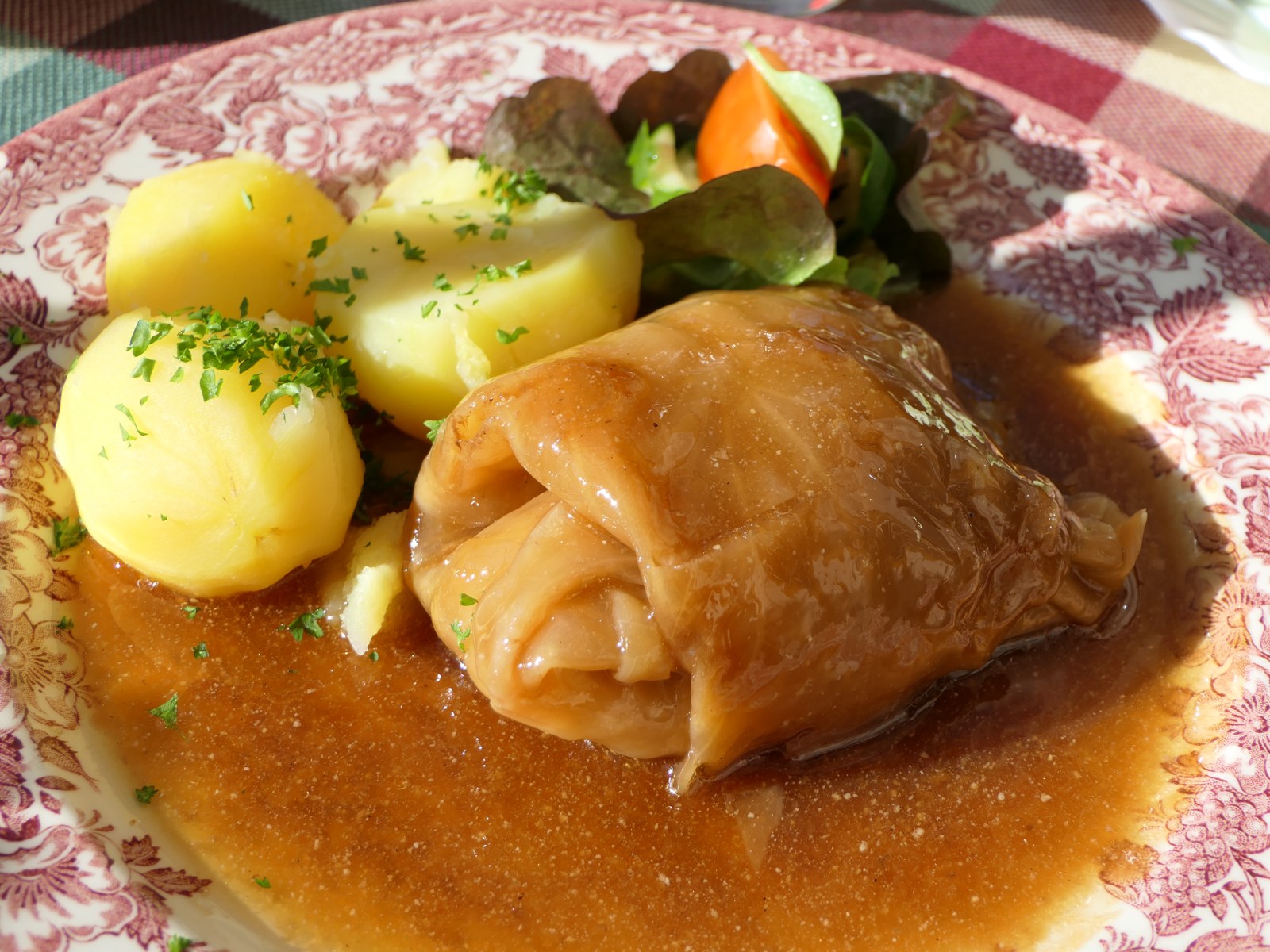 Eine gebräunte Kohlroulade mit Sauce, Kartoffeln und Gemüse