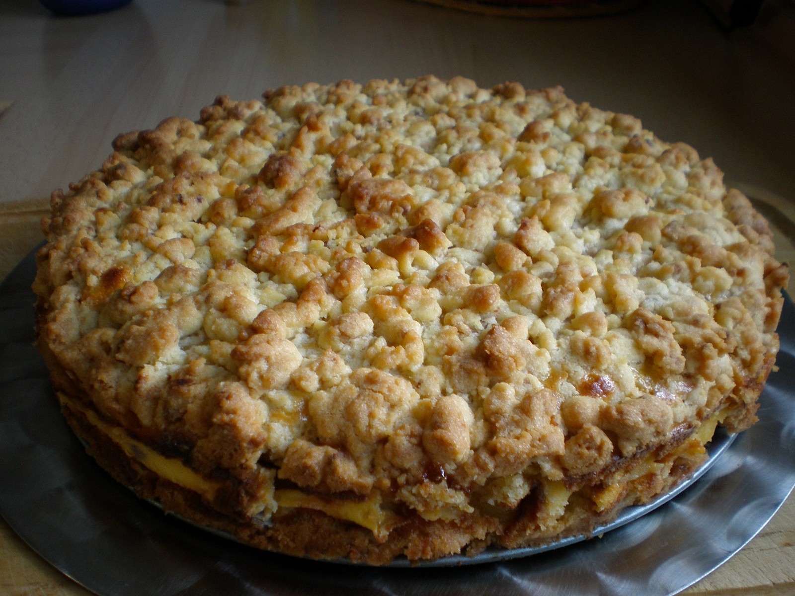 A round apple cake with golden butter streusel on a metal plate