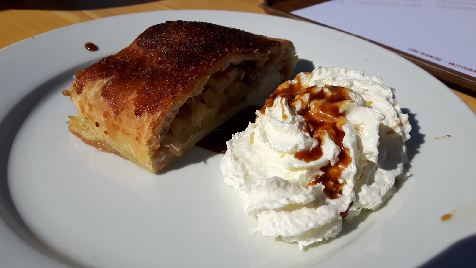 Angeschnittenes Apfelstrudelstück mit dunkler goldbrauner Hülle und Sahne