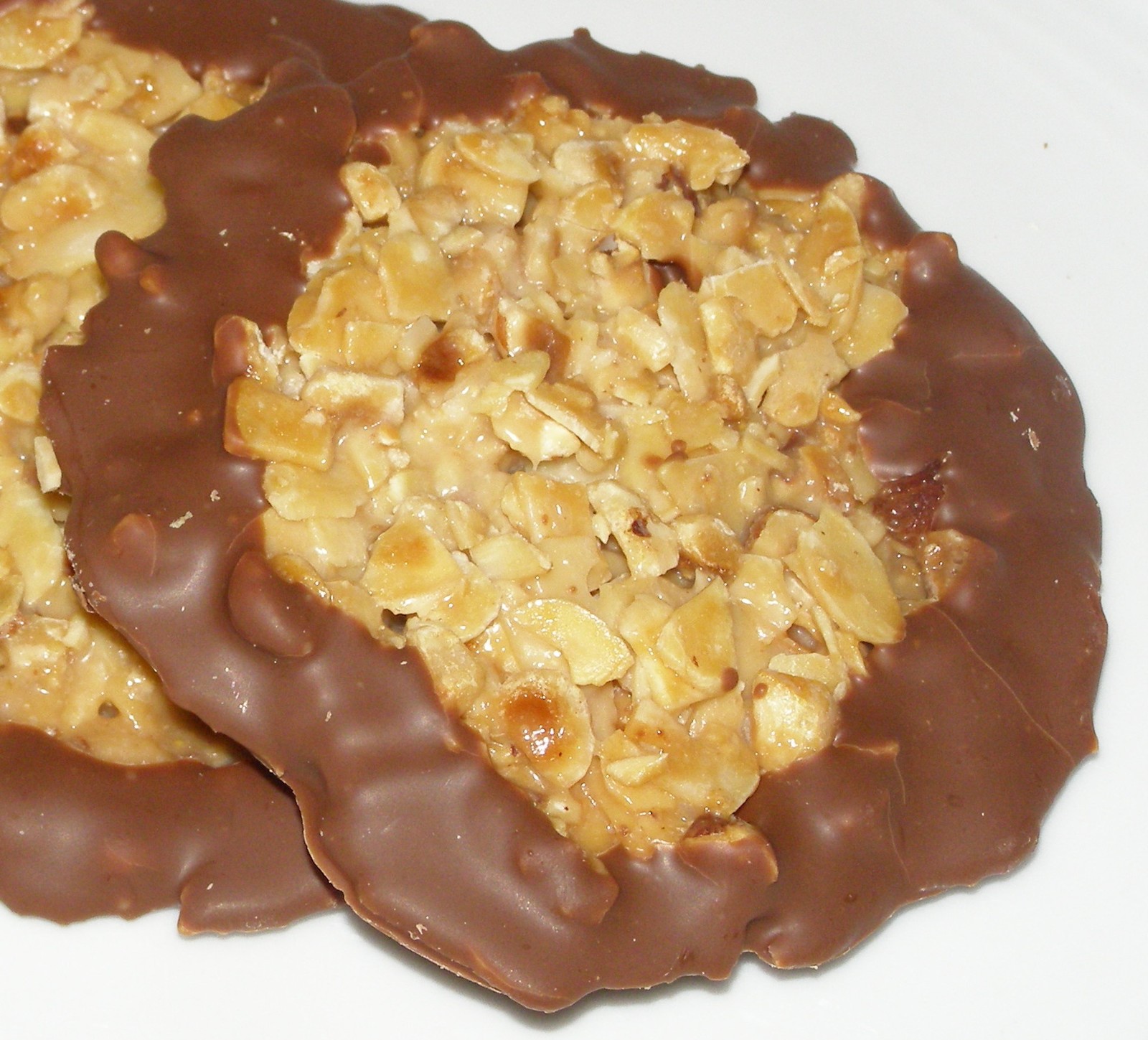 Dünne Florentiner mit Mandelblättchen und dunklen Schokoladenrändern auf einem weißen Teller