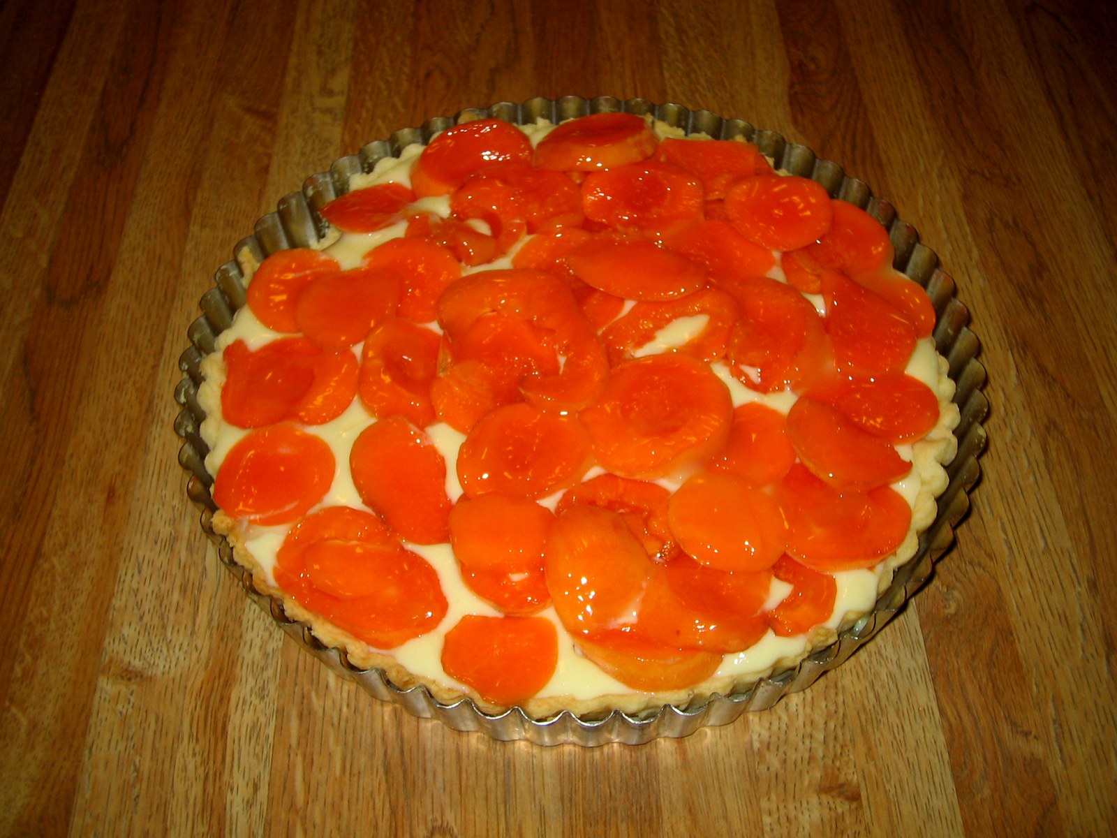 Aprikosentarte mit orangefarbenen Fruchtspalten auf heller Creme in einer geriffelten Form
